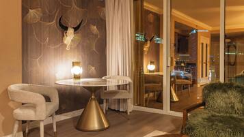 A modern hotel room with a round table, two chairs, a fur throw, and a decorative wall with a skull and ginkgo leaves.
