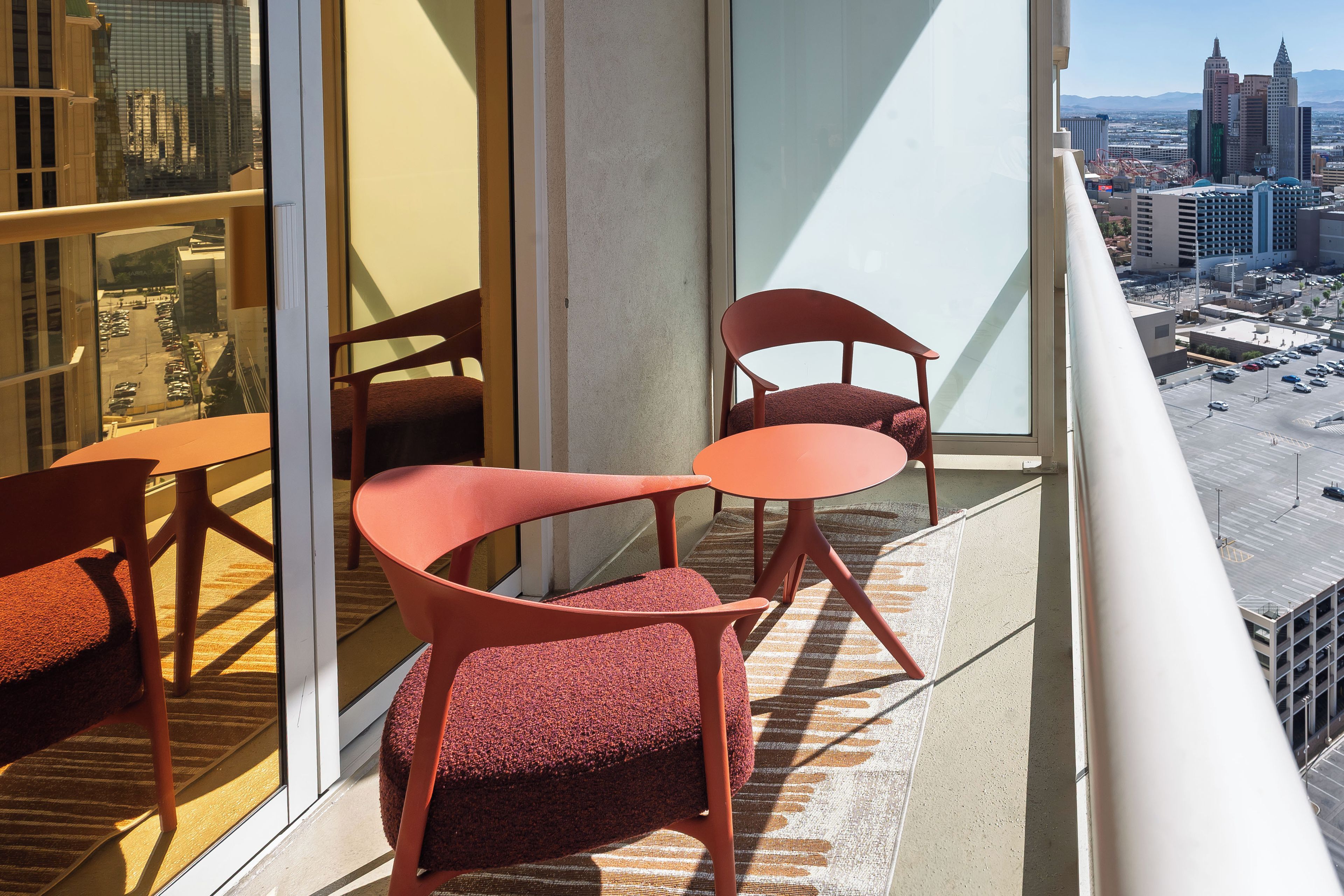A balcony with two chairs and a table, overlooking a cityscape with buildings and a parking lot.