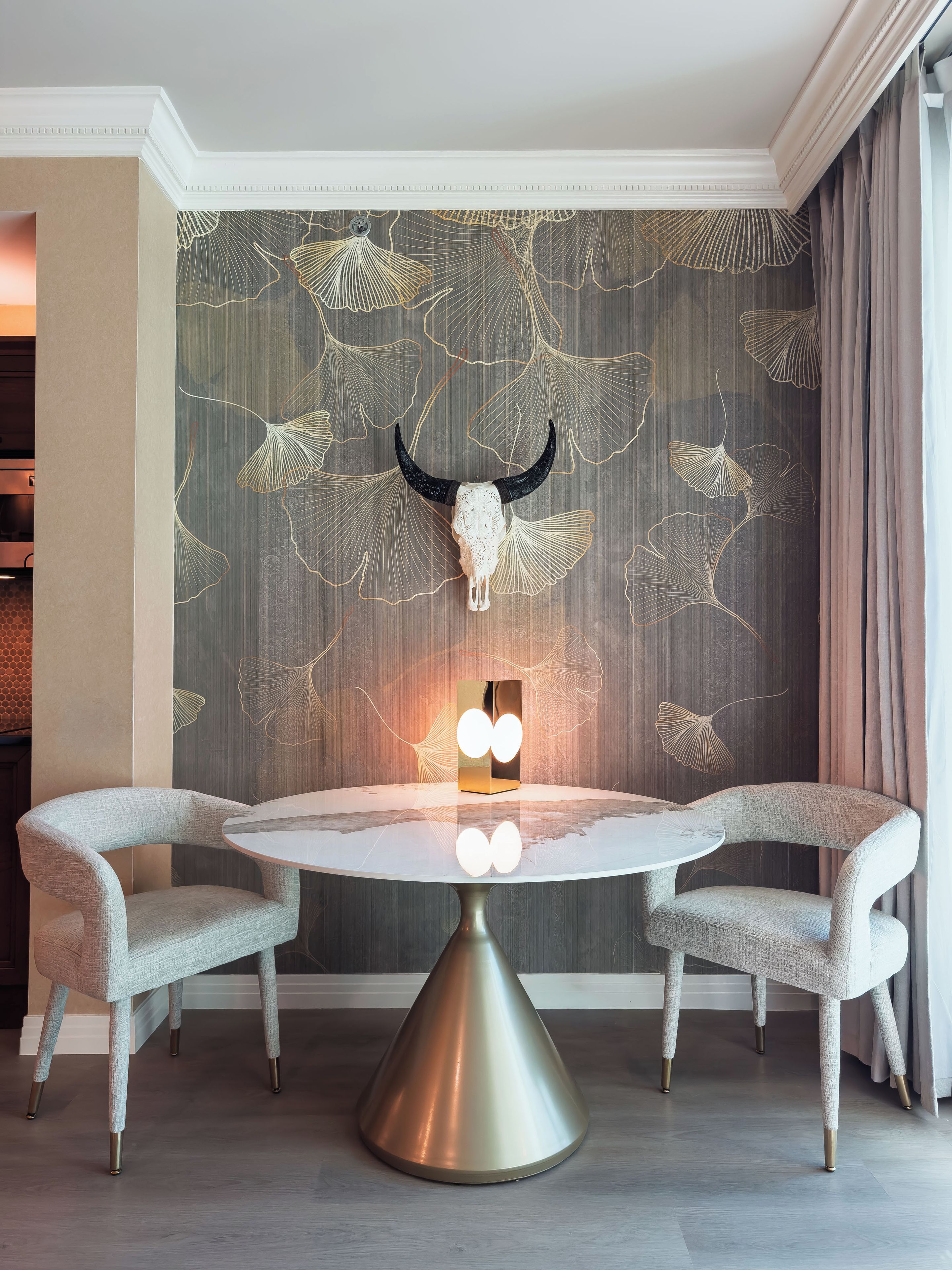 A dining area with a round table, two chairs, and a decorative wall with a bull skull and leaf patterns.