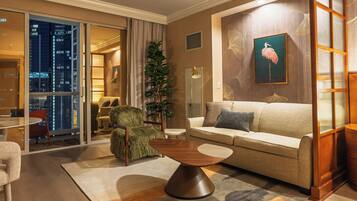 A modern living room with a sofa, armchair, and a coffee table. There is a large window with a view of the cityscape.