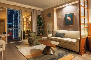 Una sala de estar moderna con un sofá, un sillón y una mesa de centro. Se ve un ventanal con vistas a la ciudad.