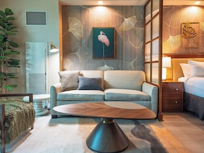A modern hotel room with a sofa, a round coffee table, a bed, and a wall with a decorative leaf pattern. - Remodeled High Floor Strip View Balcony (Las Vegas)