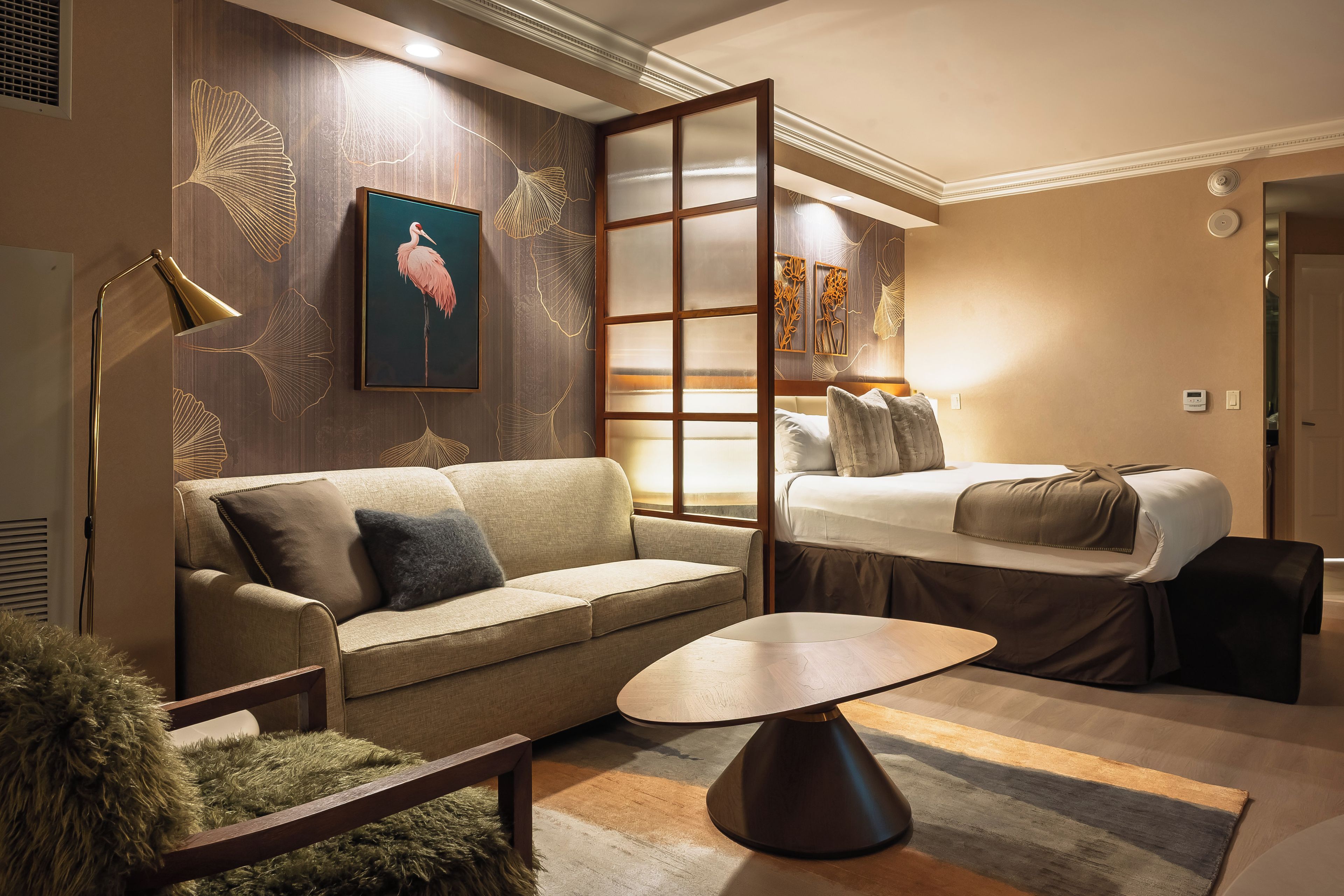 A hotel room with a sofa, a small table, a bed, and a decorative wall with a framed picture.