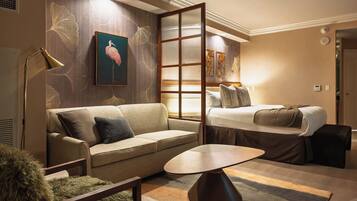 A hotel room with a sofa, a small table, a bed, and a decorative wall with a framed picture.