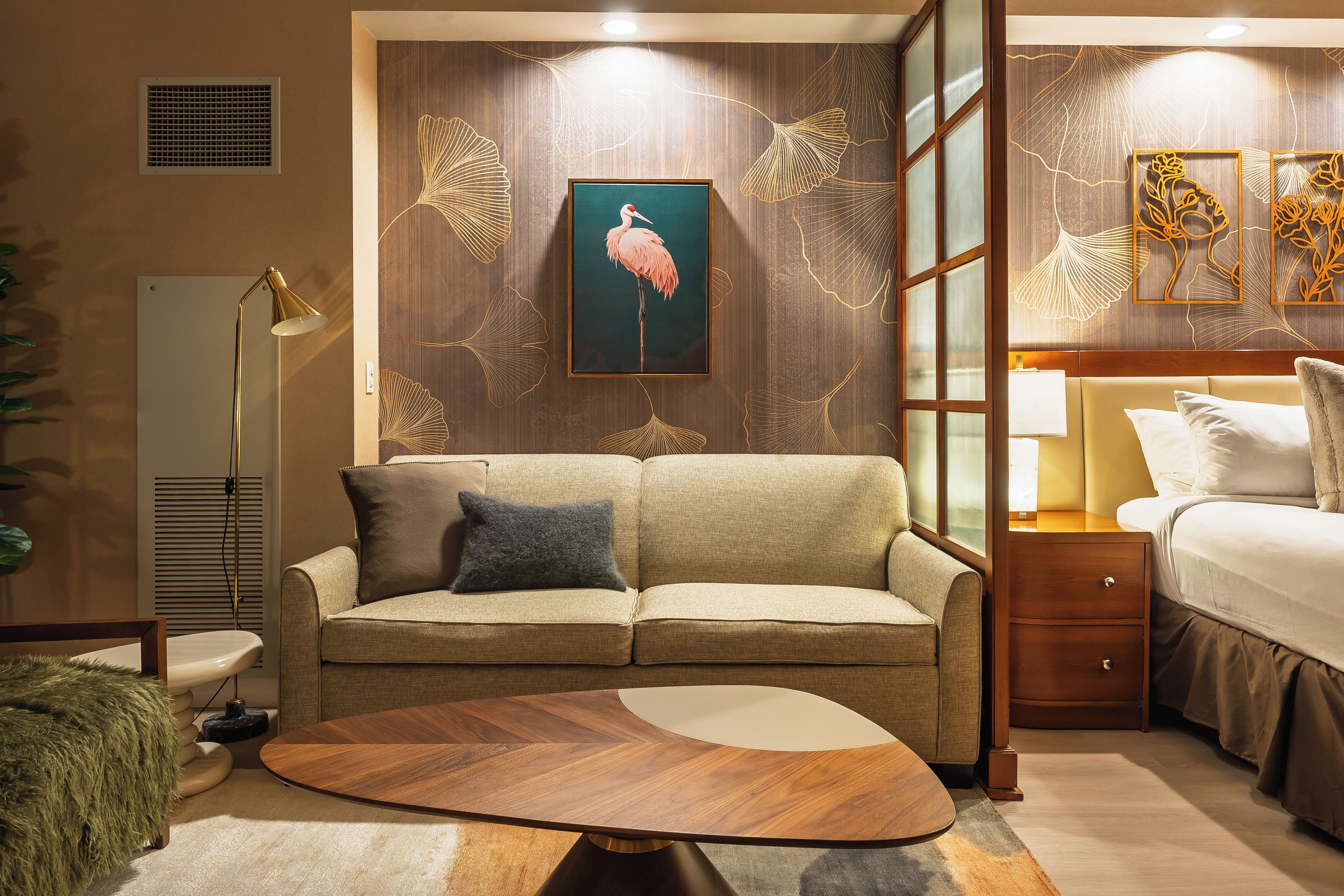 A hotel room with a sofa, a round coffee table, a bed, a bedside table, and a lamp.