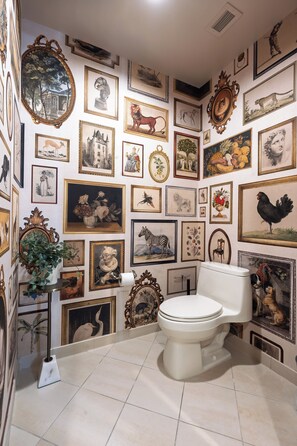 A bathroom with a toilet, surrounded by a variety of framed pictures on the walls. - Remodeled High Floor Strip View Balcony (Las Vegas)
