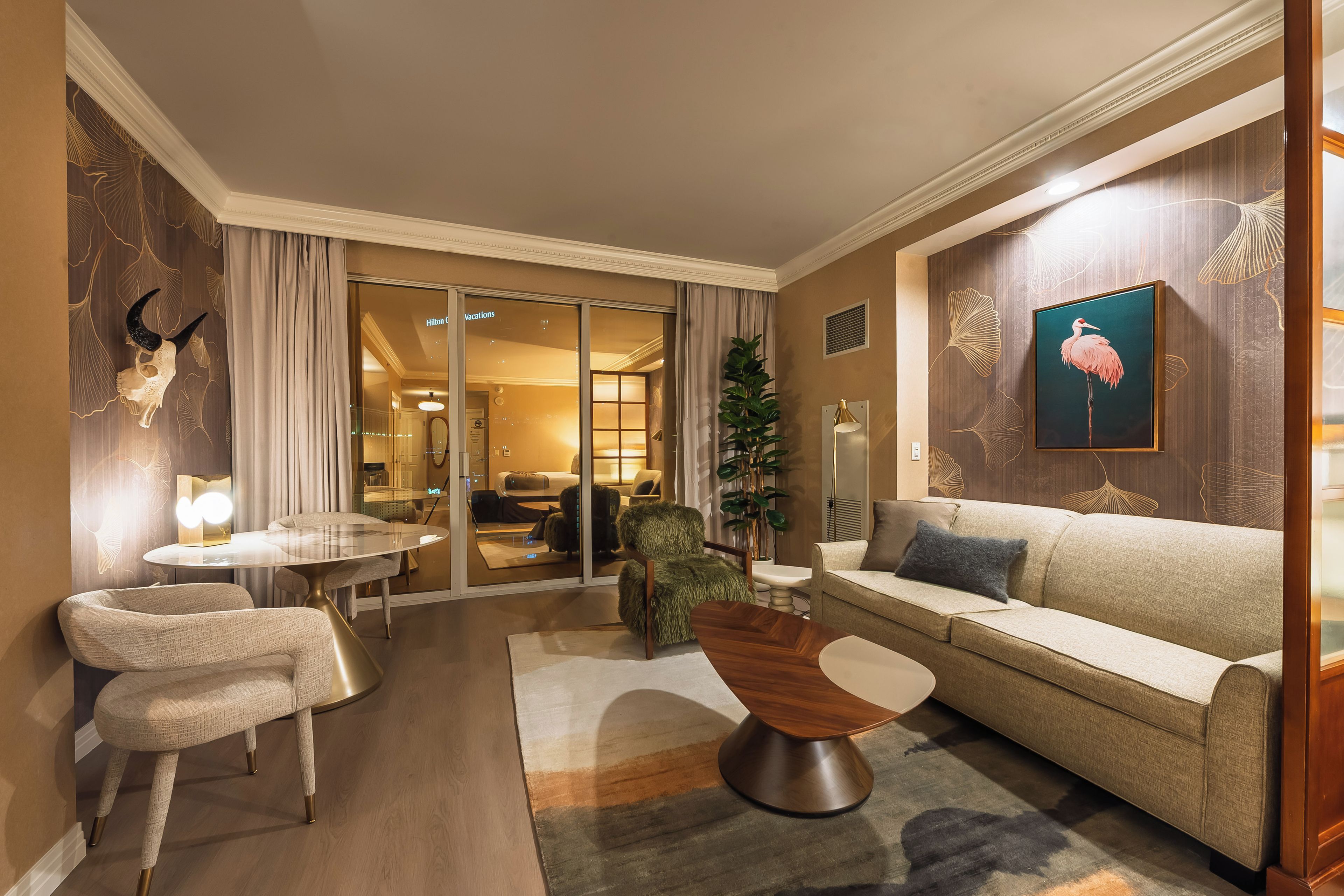Une chambre d’hôtel avec un canapé, des fauteuils, un coin repas et une vue sur l’intérieur de l’hôtel.
