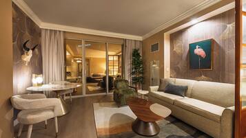 A hotel room with a sofa, chairs, a dining area, and a view into the hotel.