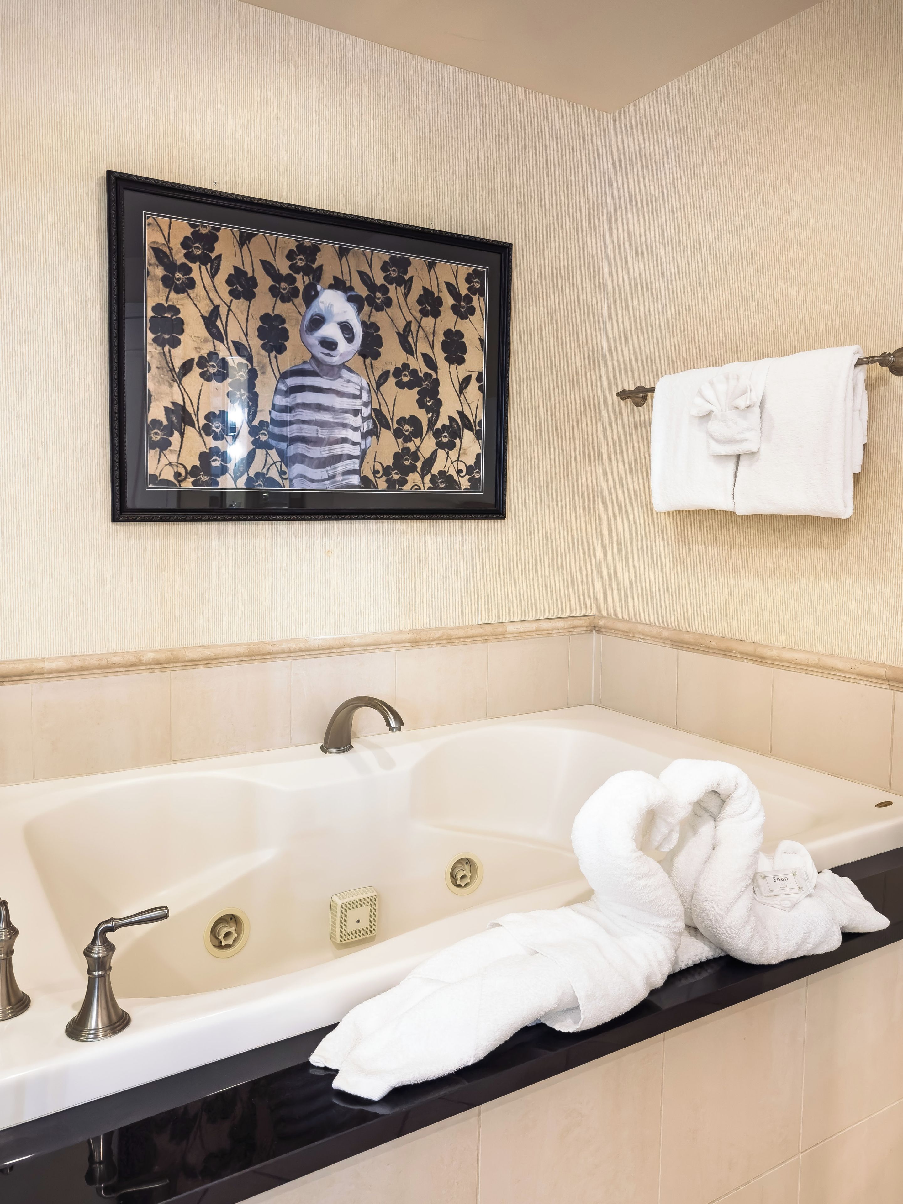 A bathroom with a large bathtub, a framed artwork above it, and a towel rack with a folded towel.