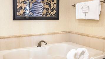A bathroom with a large bathtub, a framed artwork above it, and a towel rack with a folded towel.