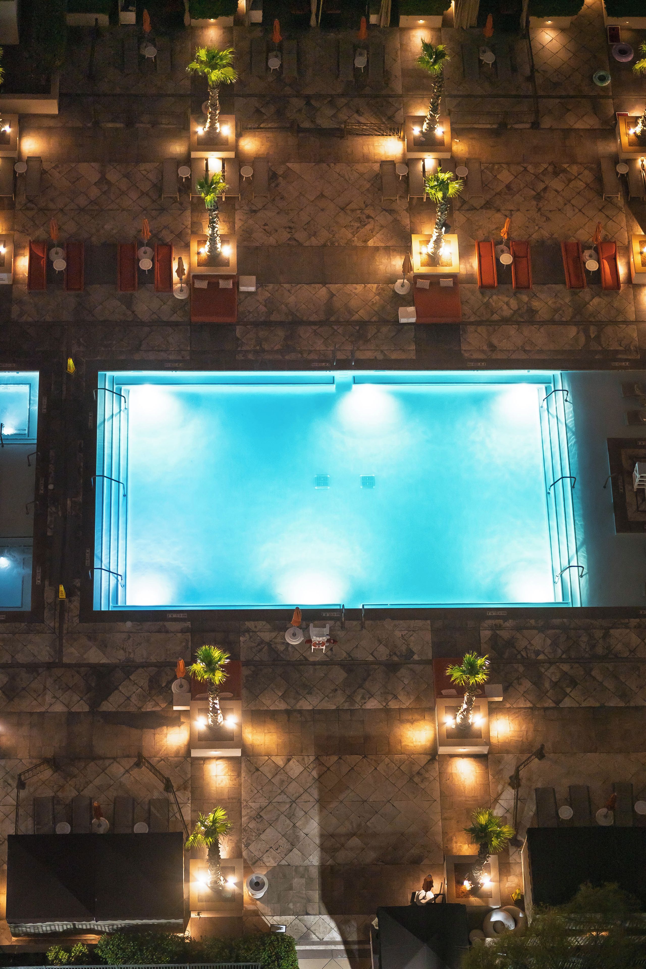 Eine Vogelperspektive auf ein Hotel mit einem rechteckigen Swimmingpool, mehreren Liegebereichen mit Sitzgelegenheiten und Topfpflanzen.