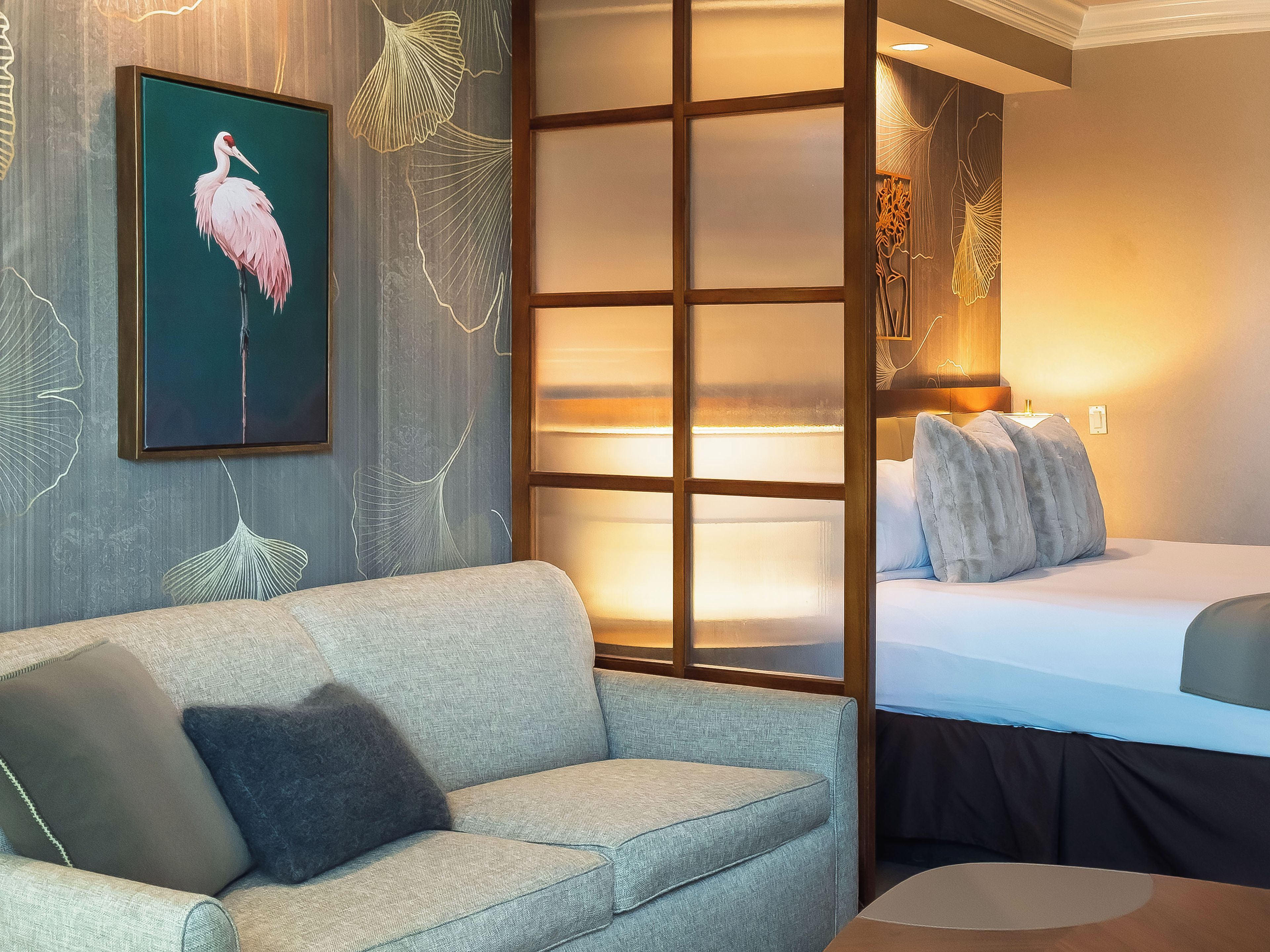 A hotel room with a sofa, a bed, and a wall with a framed artwork of a flamingo.