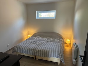 A small bedroom with a single bed, two bedside lamps, a window, and a radiator. - La Prairie Vacation Rental (Favières)