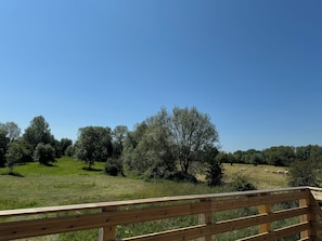 A wooden deck overlooking a grassy field with trees and a clear sky. - La Prairie Vacation Rental (Favières)