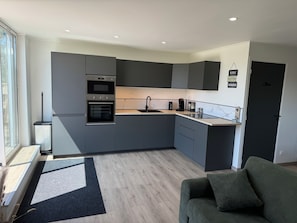 A modern kitchen with grey cabinets, a built-in oven, and a coffee machine. - La Prairie Vacation Rental (Favières)