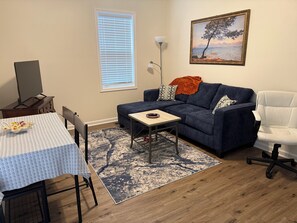 A living room with a sofa, a dining table with chairs, a TV, and a painting on the wall. - 2-bedroom, 1.5 bathroom house near UVA (Charlottesville)