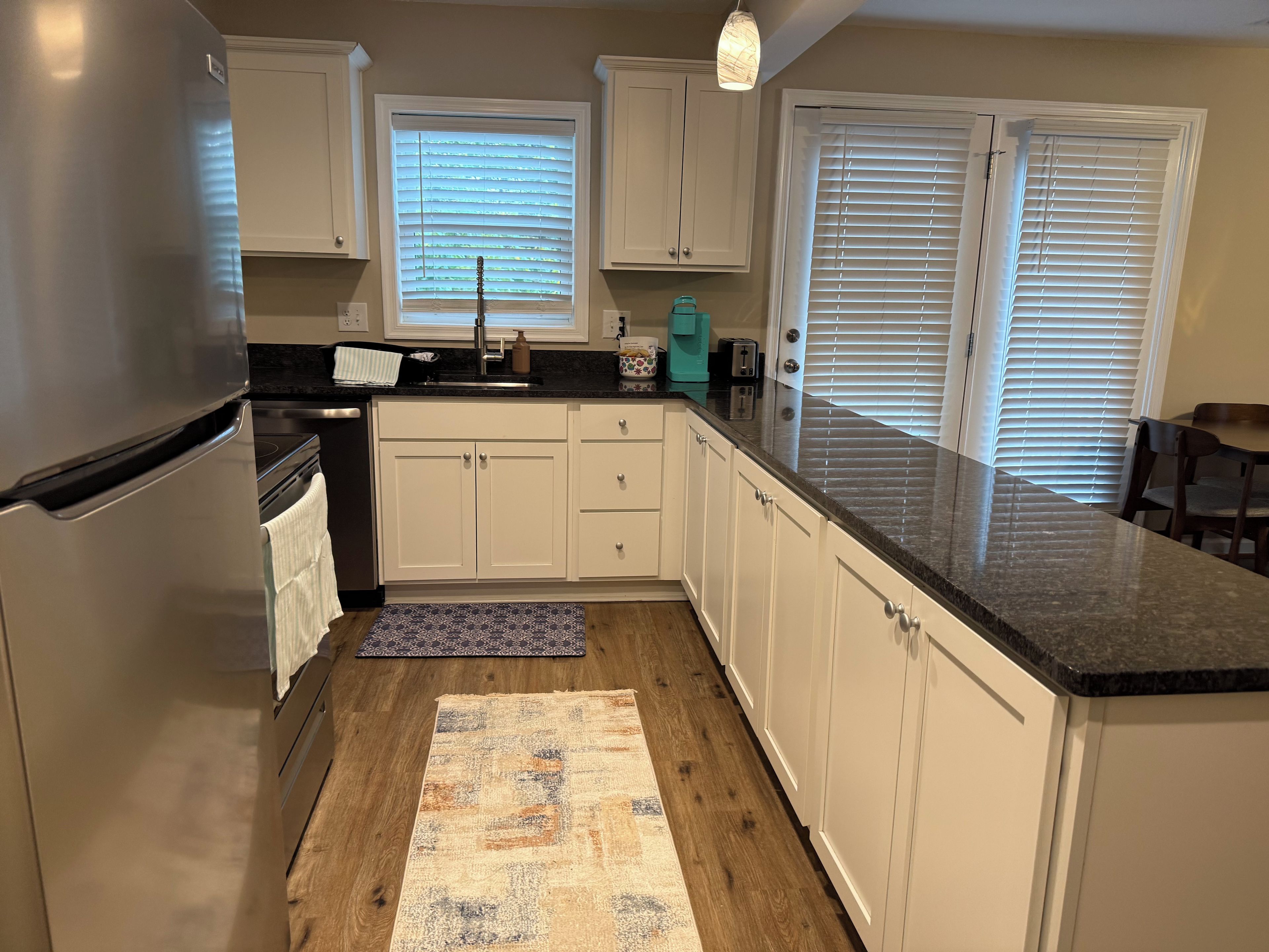 A kitchen with white cabinets, a stainless steel refrigerator, a granite countertop, and a patterned rug.