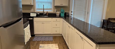 A kitchen with white cabinets, a stainless steel refrigerator, a granite countertop, and a patterned rug.