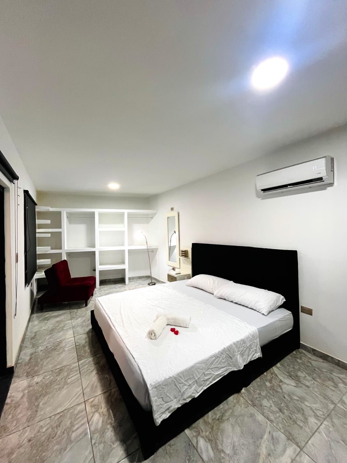 Quarto de hotel com uma cama, uma cadeira vermelha, um guarda-roupa e um aparelho de ar condicionado.