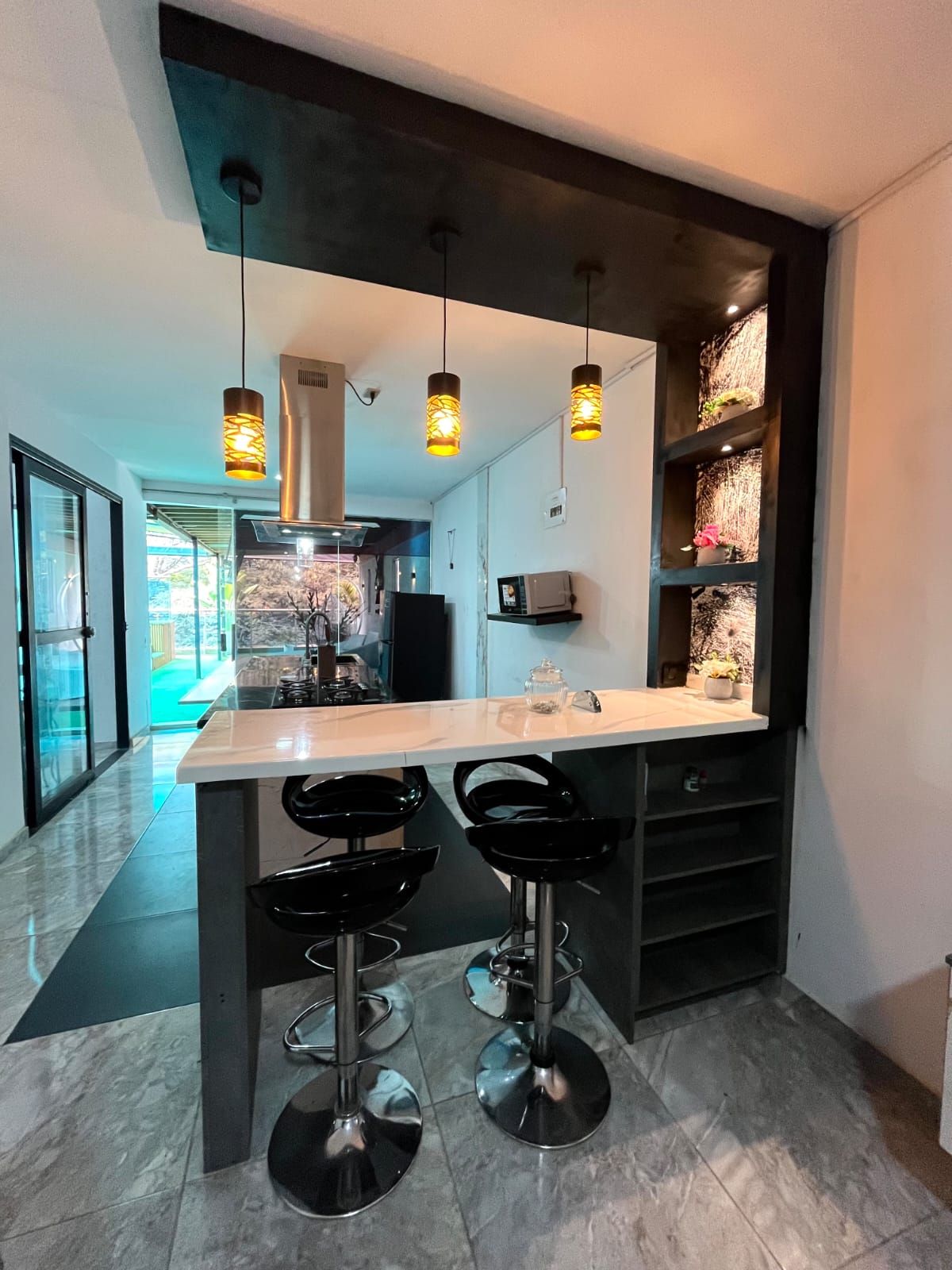 A modern kitchen with a central island, pendant lighting, and black bar stools.