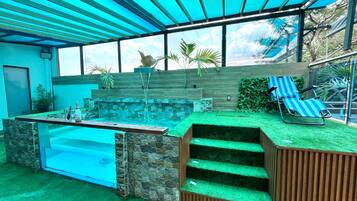 A modern outdoor pool area with a stone wall, a small waterfall feature, and a seating area with a blue-striped lounge chair.