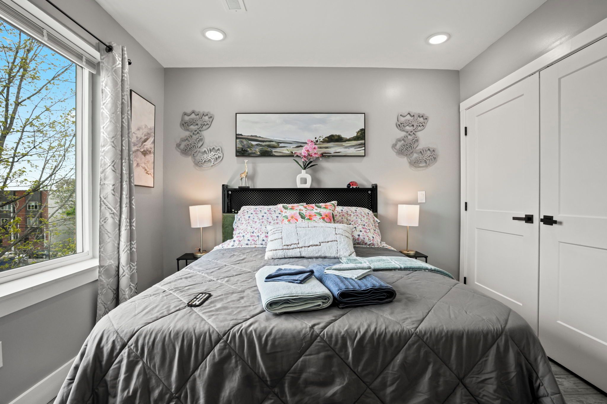 Un dormitorio con cama, dos mesitas de noche, una ventana y una puerta.