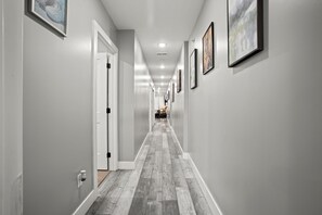 A hallway with a wooden floor, white walls, and framed artwork.