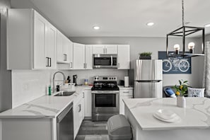 A modern kitchen with white cabinetry, stainless steel appliances, and a marble countertop.