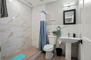 A bathroom with a shower, toilet, sink, and a mirror.