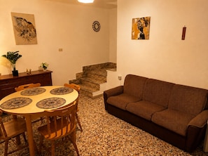 Ein Wohnzimmer mit braunem Sofa, einem Esstisch mit vier Stühlen, einer Treppe und Wandbildern.