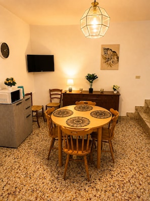Ein Essbereich mit einem runden Tisch, Stühlen, einem an der Wand befestigten Fernseher, einem Schrank und einem Boden mit einem Mosaikmuster.
