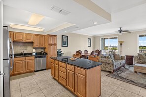 A spacious kitchen with wooden cabinets, a central island, and a dining area with a sofa and chairs. - Stone’s Throw | 3Min to Beach | Pool, Hot Tub (Mexico Beach)