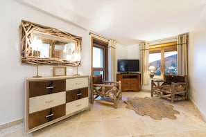 A room with a wooden dresser, a television, a rustic mirror, and a view of a mountain through a window. - Mountain lodge with pool in the Vosges (Ventron)