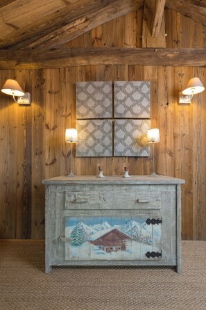 A rustic wooden interior with a wooden wall, a decorative cabinet with a winter scene, and two wall-mounted lamps. - Mountain lodge with pool in the Vosges (Ventron)