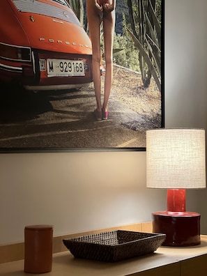 A room with a framed picture of a car, a lamp, and a woven basket on a table. - Beautiful 4-bedroom apartment on the waterfront. (le touquet paris plage)