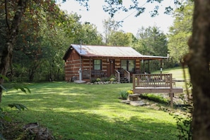 Un chalet rustique doté d’une véranda, entouré d’une pelouse bien entretenue et d’arbres.
