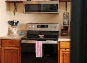 Une cuisine avec un four à micro-ondes placé au-dessus d’une cuisinière, un luminaire suspendu et un objet décoratif posé sur le plan de travail.