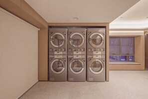 A laundry room with four stacked washing machines, a tiled floor, and a window with a view of the outside.