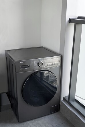 A compact, modern front-loading Haier washing machine in a corner of a room with a window.