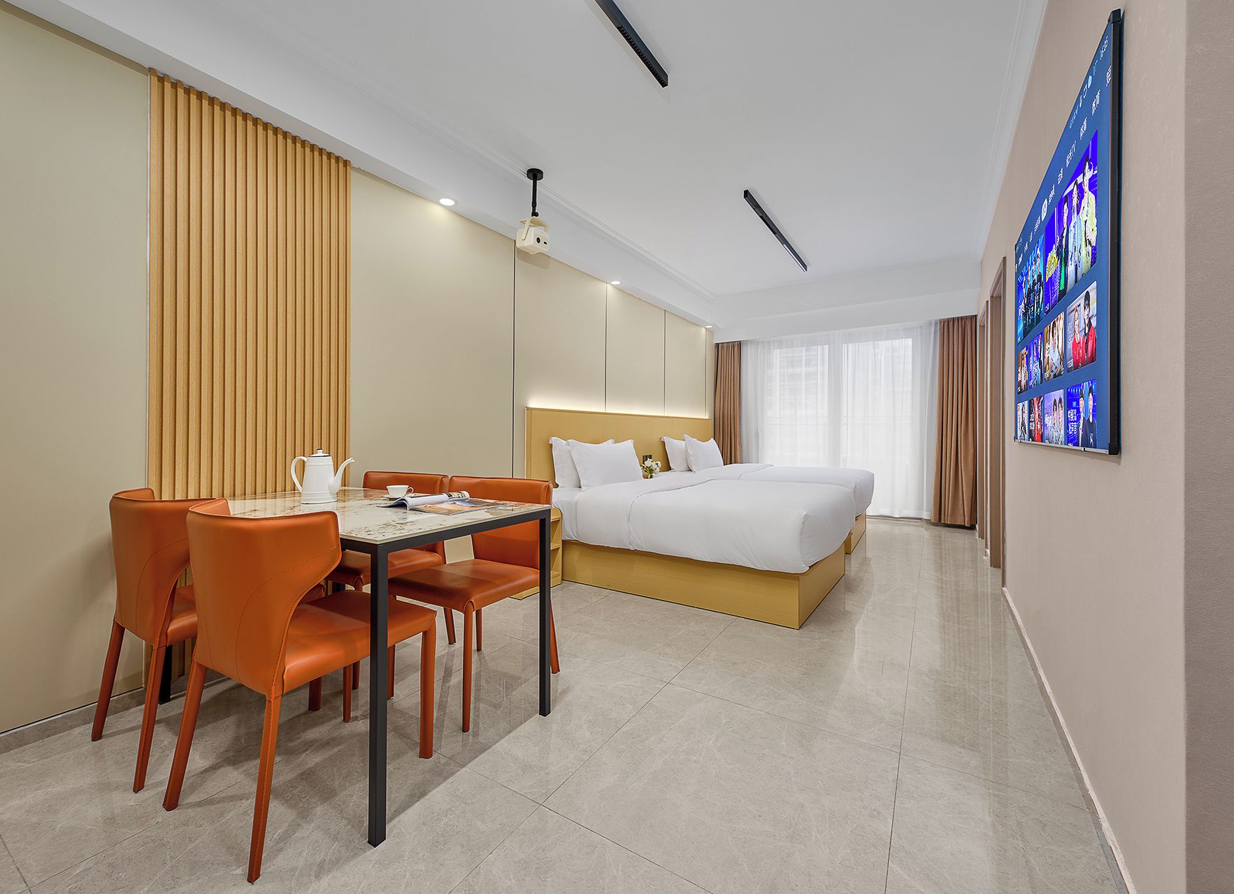 A hotel room with a bed, a dining table with chairs, a coffee table, a TV on the wall, and a large window.