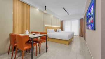 A hotel room with a bed, a dining table with chairs, a coffee table, a TV on the wall, and a large window.