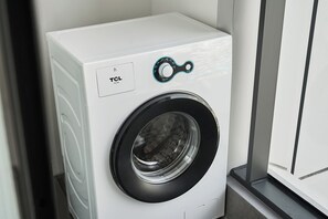 A front view of a white TCL washing machine with a front-loading door, control panel, and a circular door handle.