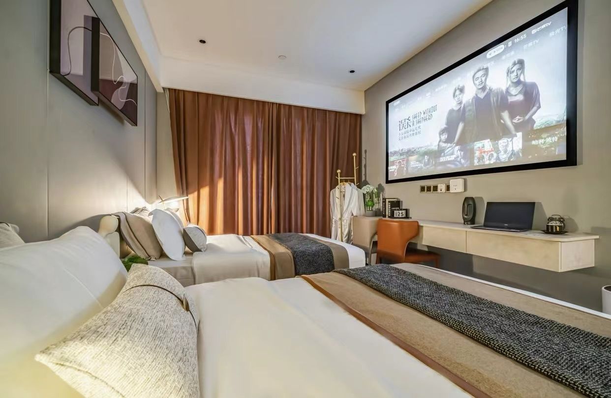 A hotel room with a bed, a desk, a television, and a large window with curtains.