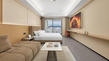 A modern hotel room with a large bed, a sofa, a coffee table, and a city view through the window.
