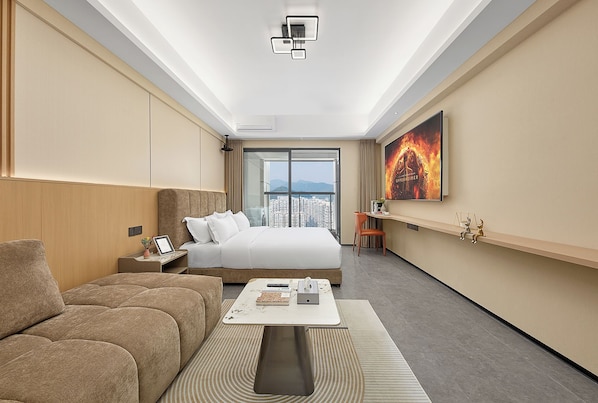 A modern hotel room with a large bed, a sofa, a coffee table, and a city view through the window.