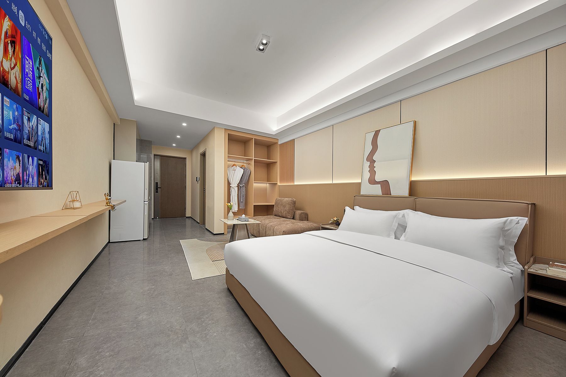 A modern hotel room with a large bed, a seating area, a wardrobe, and a wall-mounted TV.