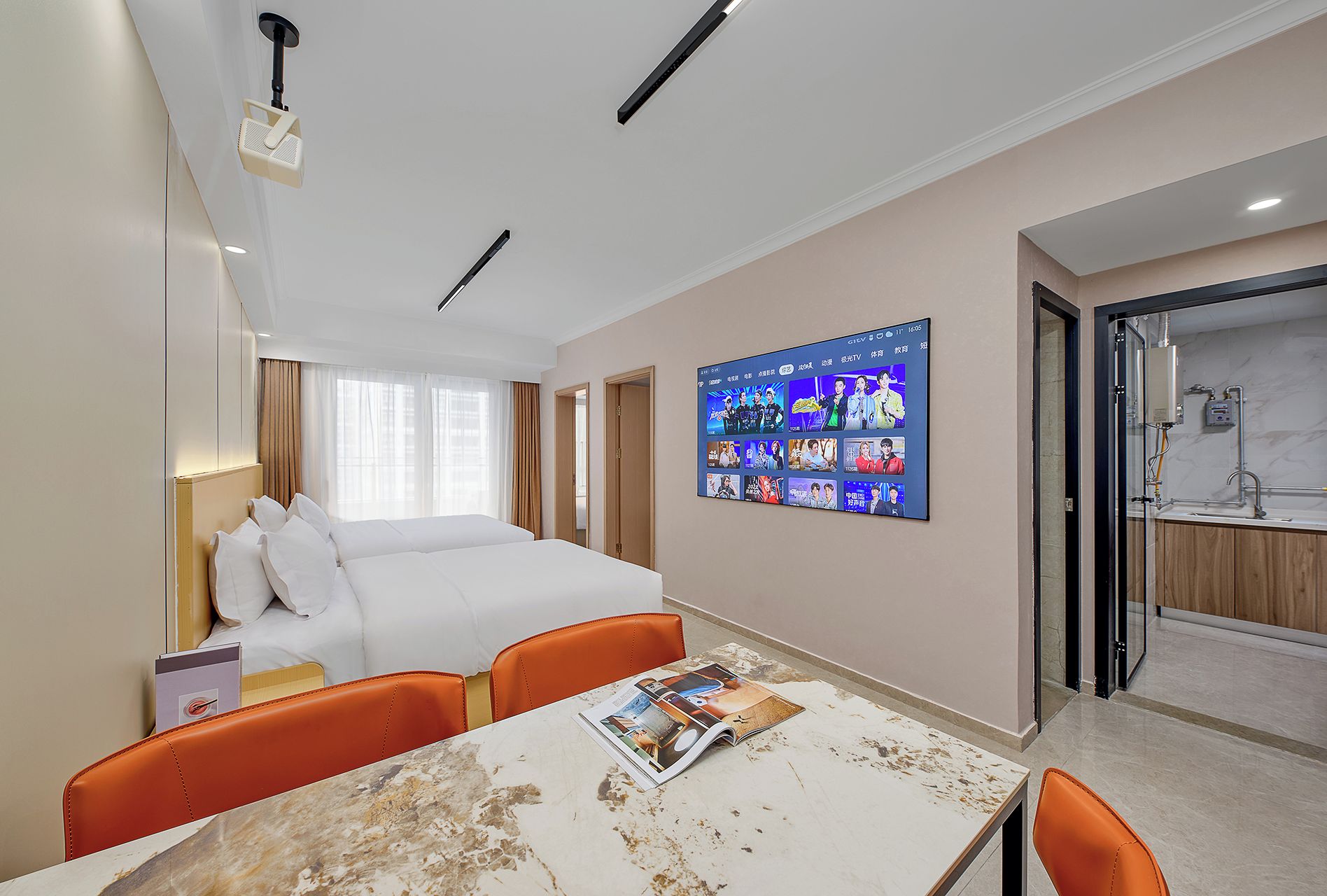 Habitación de hotel con cama, televisión montada en la pared, una mesa con una revista y un baño visible a través de una puerta abierta.