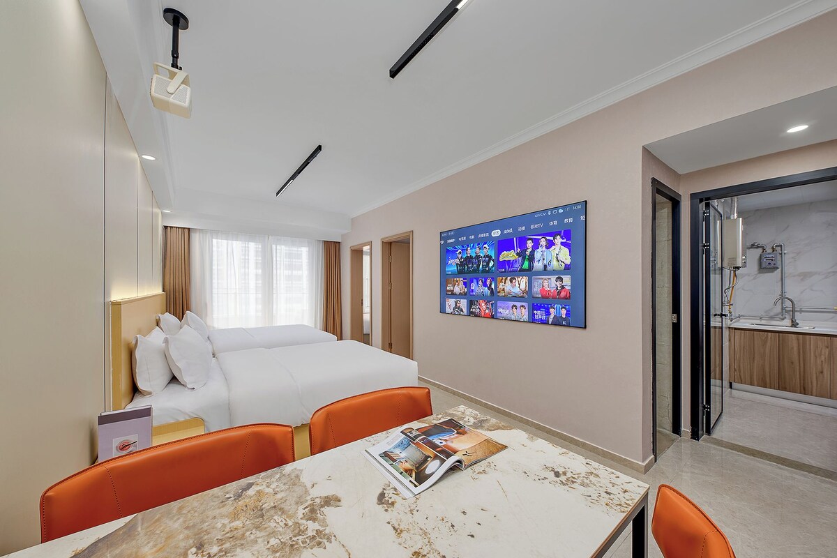 Habitación de hotel con cama, televisión montada en la pared, una mesa con una revista y un baño visible a través de una puerta abierta.