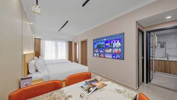 Habitación de hotel con cama, televisión montada en la pared, una mesa con una revista y un baño visible a través de una puerta abierta.