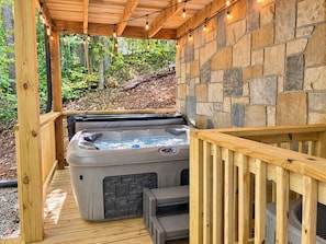 Un jacuzzi bajo una terraza de madera, con paredes de piedra y barandilla de madera.